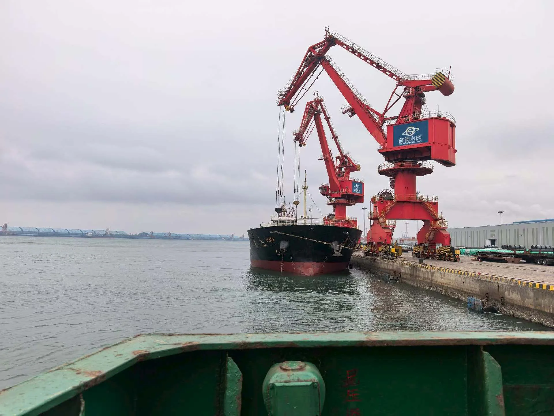 Cargo ship loading at a Chinese steel export port with CNPC cranes — bulk steel shipment overseas