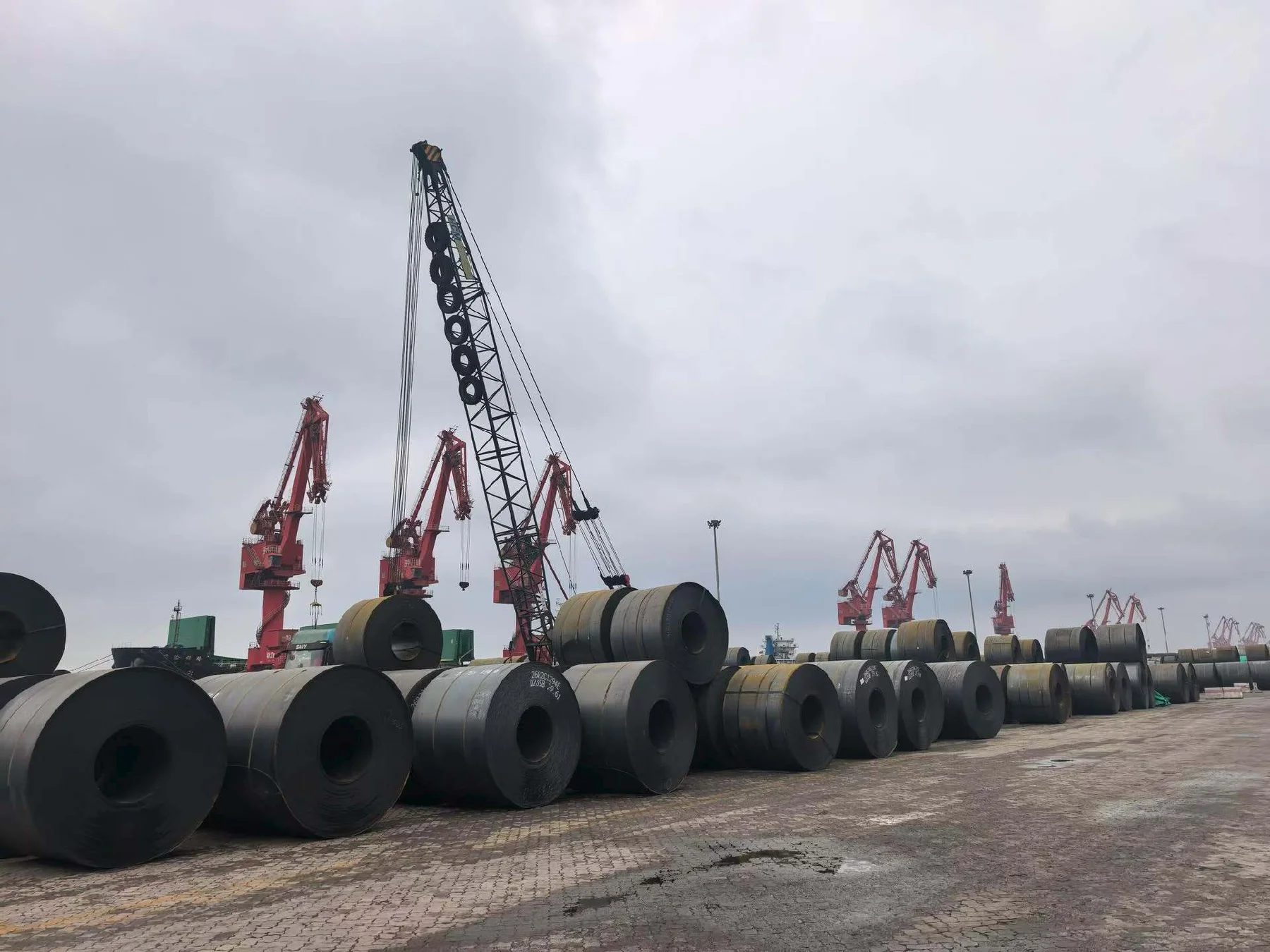 Red port cranes lifting steel coils at a Chinese export terminal — SHEDAR Steel product range